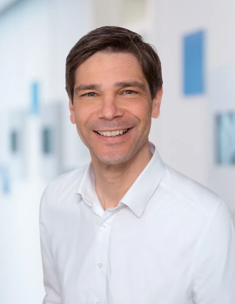 Portr&auml;t eines freundlich l&auml;chelnden Mannes in wei&szlig;em Hemd vor einem modernen, hellen B&uuml;rohintergrund. | SPIRIT/21