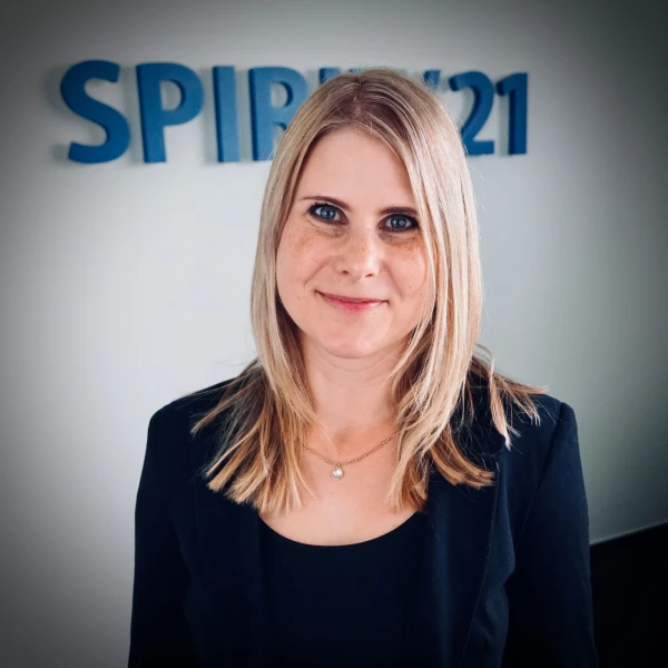 Portraitfoto einer jungen Frau mit blonden Haaren und blauen Augen, die in die Kamera l&auml;chelt. Im Hintergrund steht das SPIRIT/21-Logo | SPIRIT/21