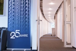 Ein langer, heller Flur mit offener T&uuml;re. Links neben der T&uuml;re steht ein Banner mit SPIRIT/21-Logo | SPIRIT/21
