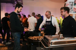 Aufnahme einer Feier. Ein Mann mit SPIRIT/21-Sch&uuml;rze sch&ouml;pft zwei weiteren M&auml;nnern Essen | SPIRIT/21