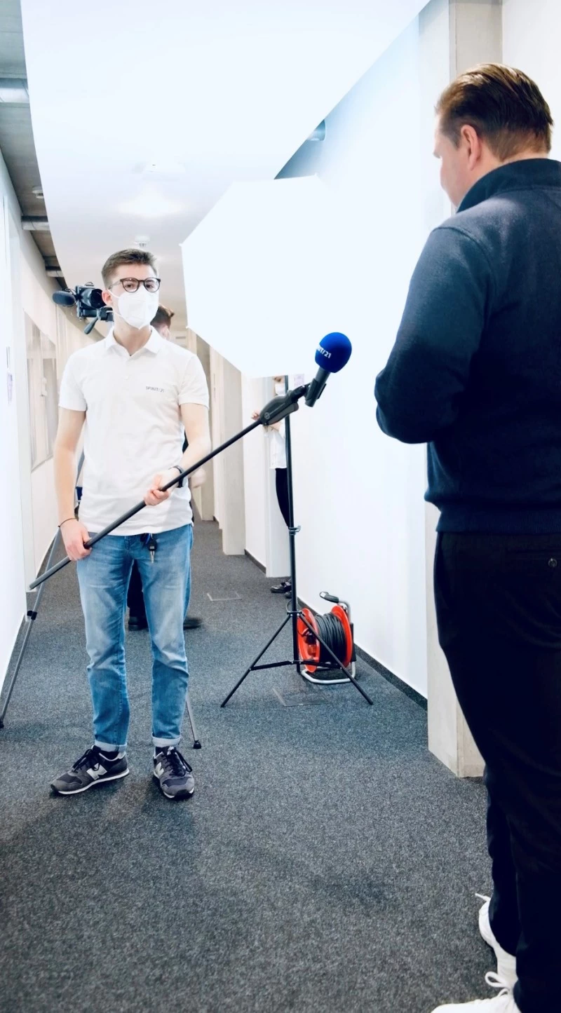 Ein Mann mit Maske h&auml;lt einem anderen Mann ein Miktofon | SPIRIT21