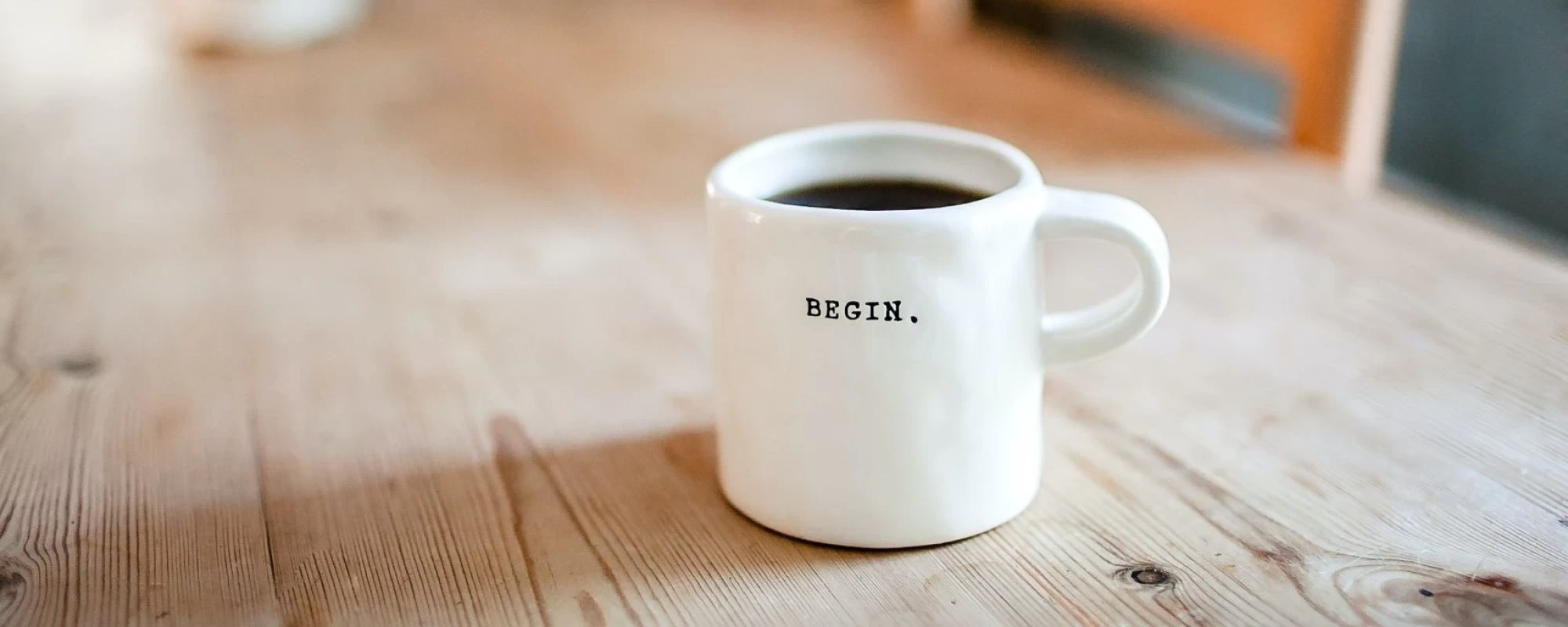 Eine wei&szlig;e Tasse auf einem Holztisch mit dem Schriftzug "Begin". | SPIRIT/21
