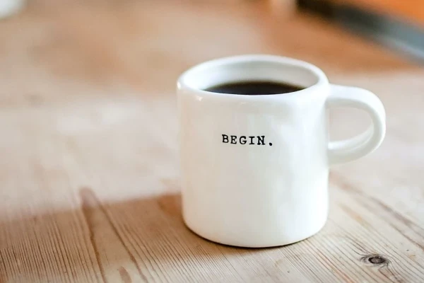 Eine wei&szlig;e Tasse auf einem Holztisch mit dem Schriftzug "Begin". | SPIRIT/21
