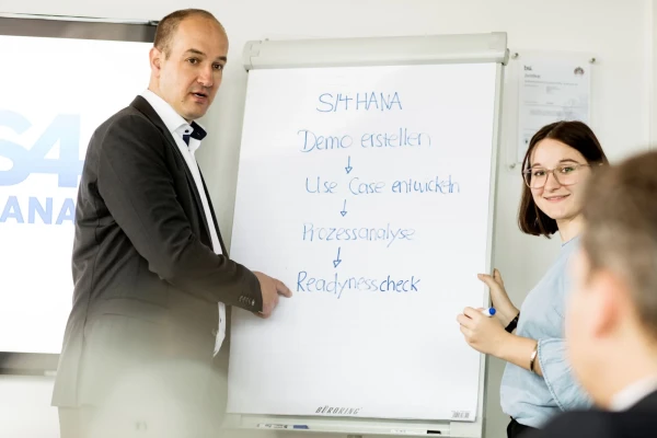 Ein Mann (links) und eine Frau (rechts) stehen vor einem Whiteboard und pr&auml;sentieren in gesch&auml;ftlichen Bereich das Thema SAP S/4HANA | SPIRIT/21